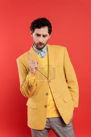 Unzufriedener Mann in gelber Jacke zeigt mit dem Finger, während Warnung isoliert auf Korallenrot 