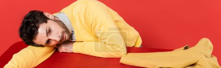 tired guy in yellow long sleeve jumper lying on red desk near blazer isolated on coral background, banner 