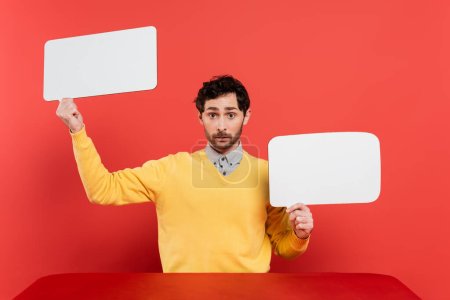 Photo for Bearded man in yellow long sleeve jumper holding blank speech bubbles on red coral background - Royalty Free Image
