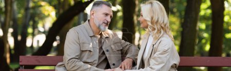 Mature man talking to blonde wife while spending time together in park, banner 