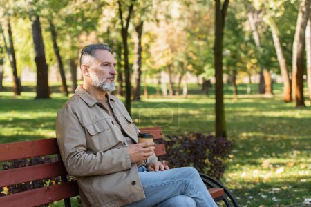 Middle aged man holding paper cup while spending time on bench in spring park 