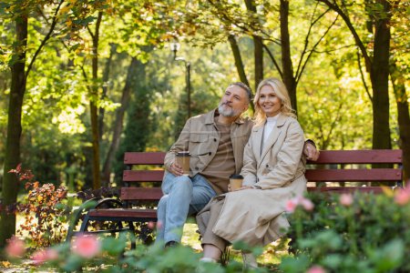 Photo for Overjoyed mature couple holding coffee to go while spending time in park - Royalty Free Image