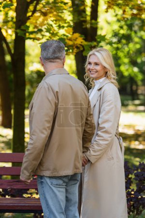 Photo for Smiling blonde woman holding hand of husband in blurred park - Royalty Free Image