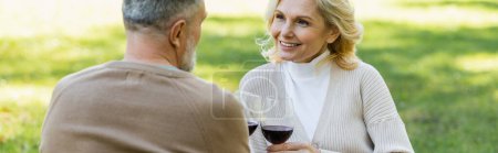 Photo for Pleased middle aged couple clinking glasses with red wine in green park, banner - Royalty Free Image