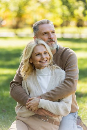 glücklicher Mann mittleren Alters mit grauem Bart umarmt charmante Frau im grünen Park 