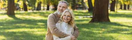Photo for Overjoyed middle aged man with grey beard hugging charming blonde wife in park, banner - Royalty Free Image