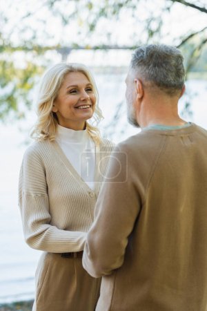 Photo for Happy middle aged woman looking at bearded husband while holding hands near lake - Royalty Free Image