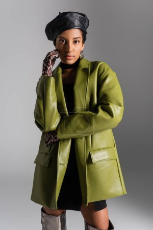 Trendy african american woman in gloves with animal print and leather coat isolated on grey 