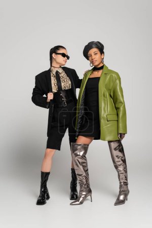 Volle Länge der multiethnischen Models im Frühlings-Outfit posiert auf grauem Hintergrund