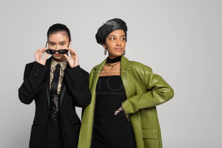 Trendy interracial models in jacket and leather coat posing isolated on grey 