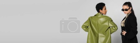 Photo for Stylish asian woman posing near african american girlfriend isolated on grey, banner - Royalty Free Image