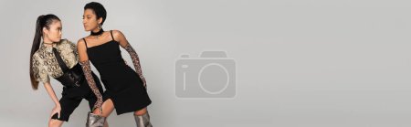 Photo pour Modèle asiatique à la mode posant avec un ami afro-américain isolé sur gris, bannière - image libre de droit