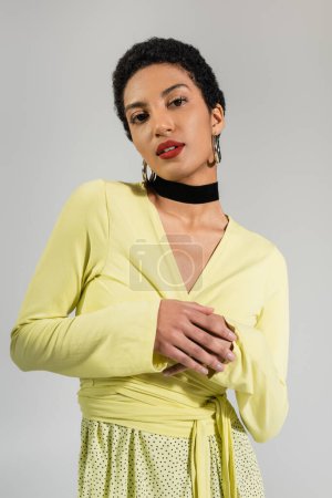 Retrato de modelo afroamericano bonito en blusa amarilla de pie aislada en gris 
