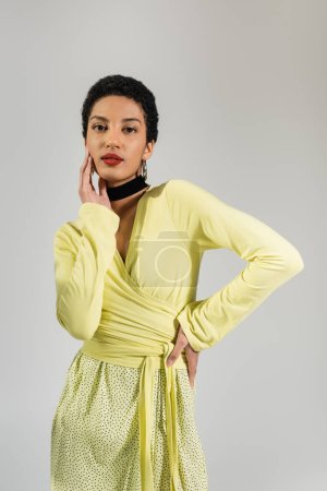 Jeune femme afro-américaine en chemisier jaune posant isolé sur gris 