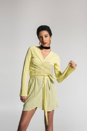 Femme afro-américaine à la mode en chemisier jaune posant isolé sur gris 