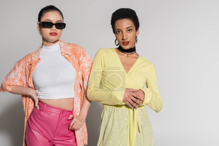 Trendy asian and african american models in spring outfit standing on grey background 