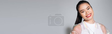 Positive asian model with red lips standing on grey background, banner 
