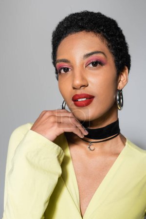 Portrait of short haired african american model with colorful makeup looking at camera on grey background 
