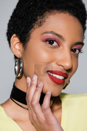 Nahaufnahme von lächelnden afrikanisch-amerikanischen Frau mit Make-up Blick auf Kamera isoliert auf grau 