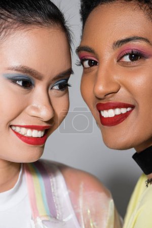 Close up view of smiling interracial models with red lips and visage on grey background 