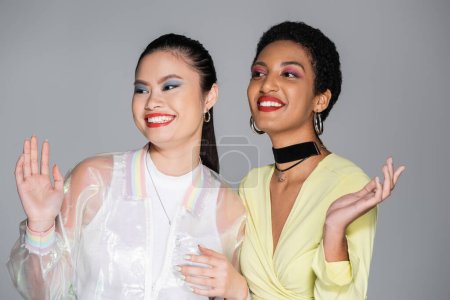 Pretty multiethnic models with red lips waving hands and smiling isolated on grey  
