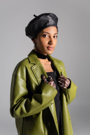 Porträt einer afrikanisch-amerikanischen Frau in Tiermusterhandschuhen und stylischem Ledermantel isoliert auf grau 