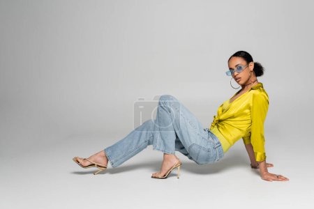 full length of stylish african american woman in high heels and trendy sunglasses posing on grey background 