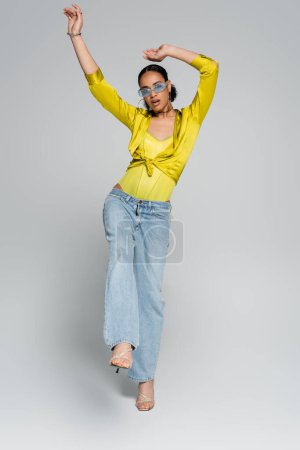 Photo for Full length of surprised african american model in trendy clothes posing on one leg on grey - Royalty Free Image