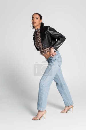 Photo for Full length of fashionable african american woman in high heeled sandals and trendy outfit walking on grey - Royalty Free Image