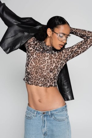 Photo for Stylish african american woman in crop top with animal print and trendy sunglasses wearing leather jacket isolated on grey - Royalty Free Image