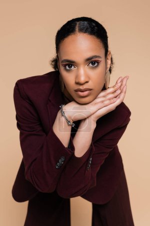 young african american woman in stylish maroon blazer posing isolated on beige 