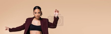 young african american woman in crop top and trendy maroon blazer posing isolated on beige, banner 