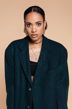Téléchargez les photos : Jeune modèle afro-américain en blazer de laine bleu foncé posant isolé sur beige - en image libre de droit