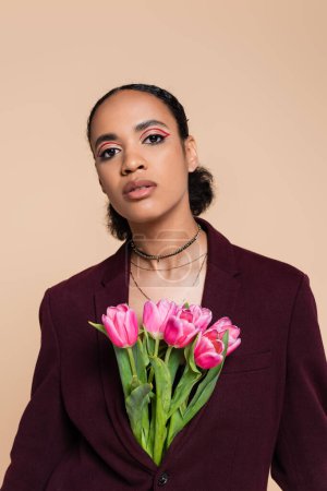 well dressed african american woman in burgundy blazer posing with pink tulips isolated on beige 