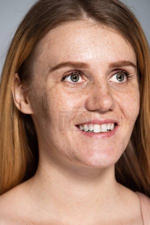 Porträt einer lächelnden Frau mit Sommersprossen im Gesicht isoliert auf grau 