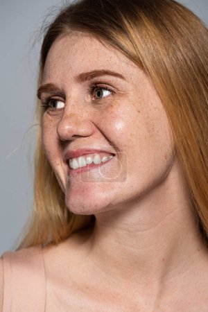 Fröhliche junge Frau mit Hautproblem schaut vereinzelt auf grau 