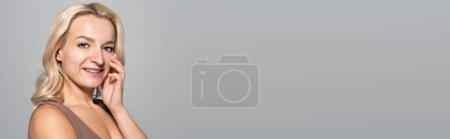 Photo for Pretty woman with acne on face touching skin isolated on grey, banner - Royalty Free Image