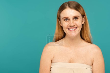 Smiling freckled woman looking at camera isolated on turquoise