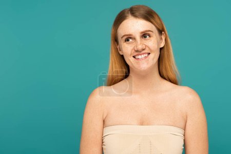 Overjoyed woman with freckles looking away isolated on turquoise