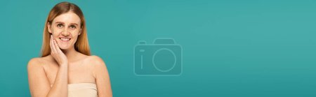 Positive young woman with freckles standing isolated on turquoise, banner 