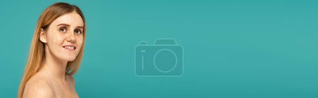 Photo for Young woman with freckled skin and naked shoulders looking at camera isolated on turquoise, banner - Royalty Free Image