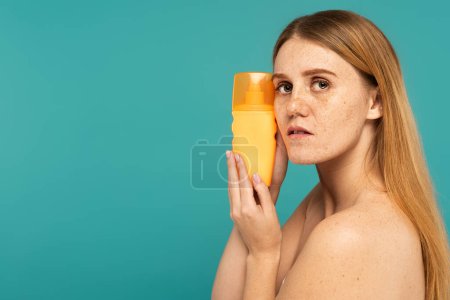 Junge Frau mit Sommersprossen auf der Haut hält Sonnencreme isoliert auf Türkis