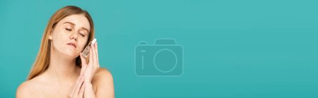 Photo for Redhead woman with freckles and closed eyes holding serum in bottle isolated on turquoise, banner - Royalty Free Image