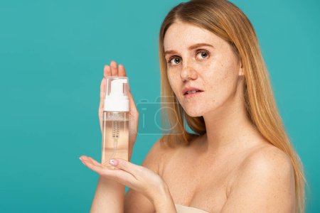Téléchargez les photos : Jeune rousse femme aux taches de rousseur tenant bouteille avec nettoyant mousse isolé sur turquoise - en image libre de droit