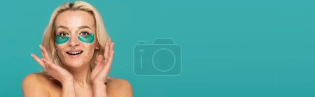 amazed woman with acne and moisturizing eye patches smiling isolated on turquoise, banner 
