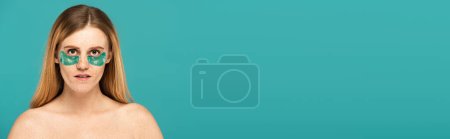 Photo for Redhead woman with freckles and patches under eyes looking at camera isolated on turquoise, banner - Royalty Free Image