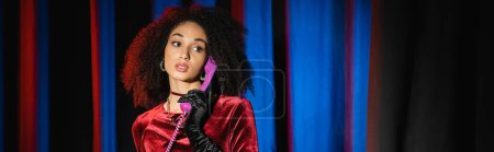 Téléchargez les photos : Femme afro-américaine élégante en gant de velours parlant au téléphone sur fond bleu avec lumière, bannière - en image libre de droit
