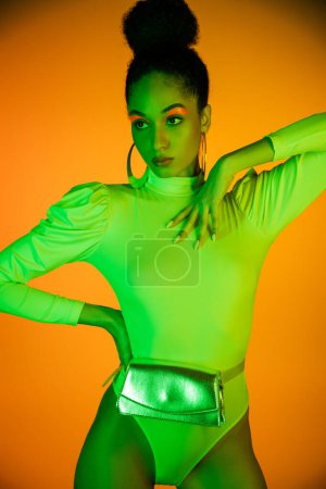 Trendy afrikanisch-amerikanische Frau in Neon-Body und Make-up posiert auf orangefarbenem Hintergrund 