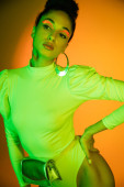 Fashionable african american model with neon visage posing in bodysuit on orange background  puzzle #648332606