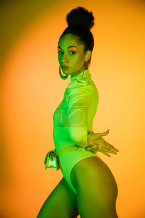 Sexy afrikanisch-amerikanisches Model im neonfarbenen Body schaut in die Kamera auf orangefarbenem Hintergrund 
